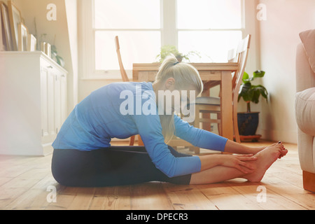 Junge Frau sitzt am Boden schiefe Zehen nach vorne berühren Stockfoto