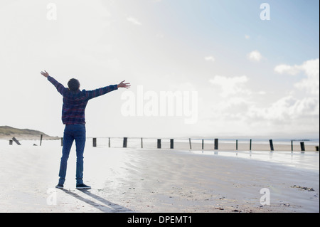 Junge Mann stand am Strand mit Armen, Brean Sands, Somerset, England Stockfoto