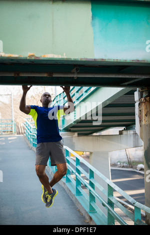 Mann tut Pull ups auf Brücke Stockfoto
