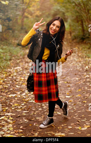 Junge Frau im Park, anhören von Musik über Kopfhörer, making Peace-Zeichen Stockfoto