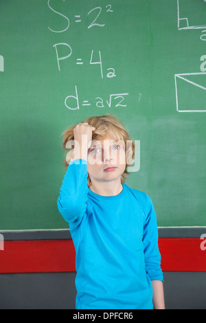 Traurig Schuljunge stehend gegen Brett im Klassenzimmer Stockfoto