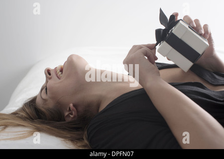 Junge Frau auf dem Bett liegend mit Geschenk Stockfoto