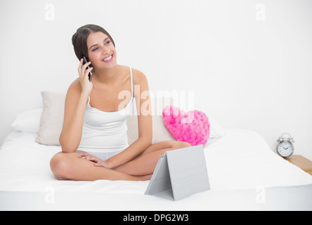 Verträumte junge braun behaart Modell in weißen Schlafanzug telefonieren Stockfoto