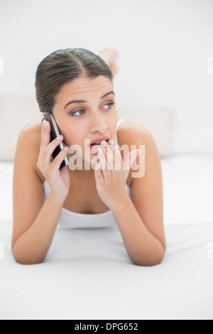 Schockiert jungen braunen Haaren Modell in weißen Schlafanzug mit ihrem Handy aufrufen Stockfoto