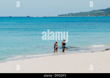 Zwei Afrikanische amerikanische Frauen, die floatation Geräte vom Karibischen Meer auf den Strand in St. Croix Wade. Frederiksted Pier im Hintergrund. Stockfoto