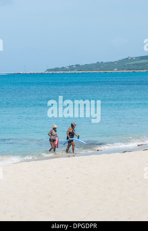 Waten Sie zwei afroamerikanische Frauen, Flotation Geräte vom karibischen Meer an den Strand in St. Croix Stockfoto