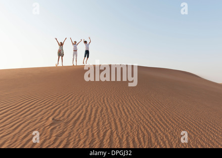 Kinder springen auf Düne mit Luft erhobenen Armen Stockfoto