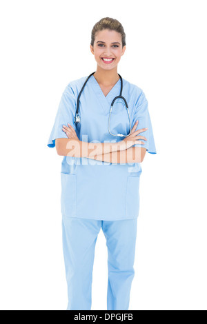 Lächelnd braunen Haaren Krankenschwester in blau scheuert posiert mit verschränkten Armen Stockfoto