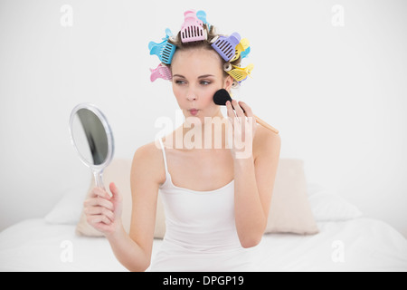 Schmollend natürliche braune kurzhaarige Frau in Lockenwicklern Auftragen von Puder im Gesicht Stockfoto