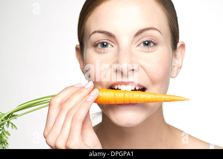 Junge Frau beißen in Karotten, Porträt Stockfoto