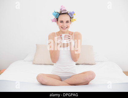 Ziemlich natürlich braune kurzhaarige Frau in Lockenwicklern hält eine Tasse Kaffee Stockfoto