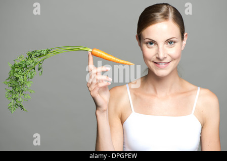 Junge Frau Karotte am Fingerspitze Abwägung Stockfoto