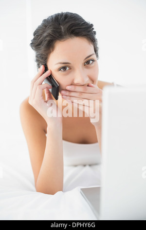 Schockiert lässig Brünette in weißen Schlafanzug telefonieren Stockfoto
