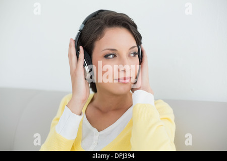 Nachdenklich lässig Brünette in gelbe Strickjacke Musikhören mit Kopfhörer Stockfoto