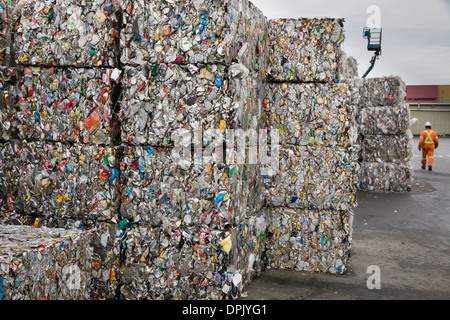 Ein Arbeiter geht vorbei an gestapelten Kuben aus aus zerkleinerten Metalldosen, die Versandkosten zu einer Recyclinganlage besitzen zu erwarten. Stockfoto