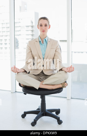 Konzentrierte sich schicke Geschäftsfrau sitzen im Lotussitz auf ihrem Drehstuhl Stockfoto