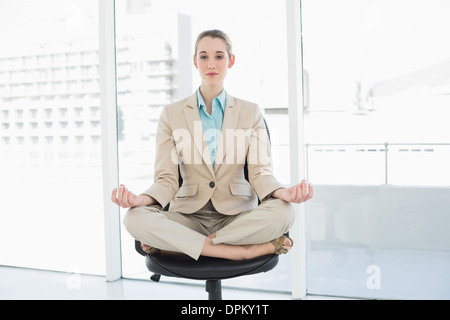 Schöne elegante Geschäftsfrau sitzen im Lotussitz auf ihrem Drehstuhl Stockfoto