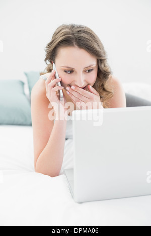 Lächelnde Frau mit Handy und Laptop im Bett Stockfoto