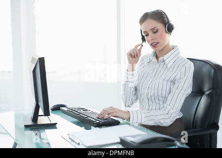 Konzentrierte sich schöne Agent tragen Kopfhörer sitzt an ihrem Schreibtisch Stockfoto