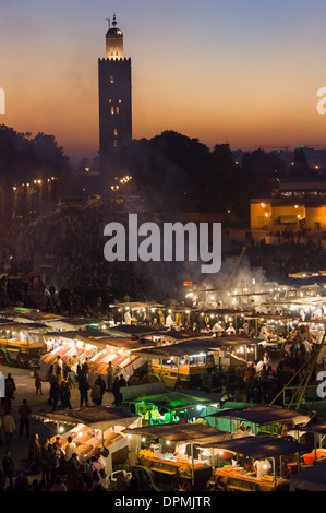 Essensstände in dem Djemaa el-Fna Platz bei Sonnenuntergang, mit der Silhouette des das Minarett der Koutoubia-Moschee, Marrakesch, Marokko Stockfoto