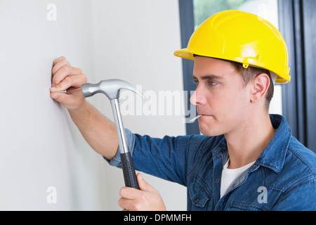 Handwerker hämmern Nagel in Wand Stockfoto