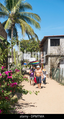 Menschen gehen sandigen Weg hinunter zum Strand, gesäumt von Palmen & schöne blühende Bougainvillea im malerischen Küstenstadt Stockfoto