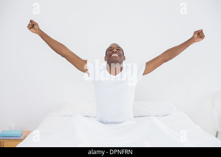 Lächelnder Afro Mann streckte seine Arme im Bett Stockfoto