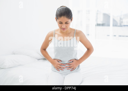 Lässige Frau mit Magenschmerzen im Bett sitzen Stockfoto