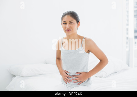 Lässige Frau mit Magenschmerzen im Bett sitzen Stockfoto