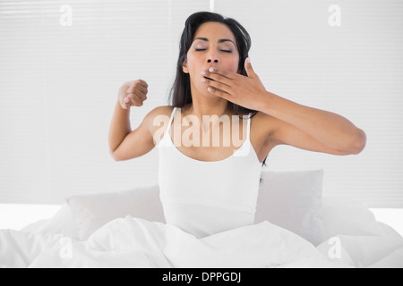 Nette junge Frau Gähnen beim Sitzen auf ihrem Bett Stockfoto