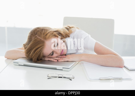 Müde Geschäftsfrau mit Kopf auf Laptop im Büro Stockfoto