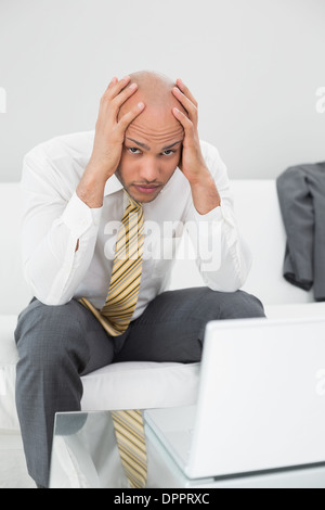 Besorgt Geschäftsmann mit Laptop mit Kopf in Händen zu Hause Stockfoto