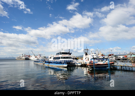 Ushuaia Port Tour Boats Kreuzfahrt Frachtschiffe Ushuaia Argentinien | USHUAIA, Argentinien — Kleine lokale Tourboote liegen im Hafen von Ushuaia vor Anker, während große transozeanische Kreuzfahrtschiffe und Frachtschiffe im Hintergrund zu sehen sind. Ushuaia liegt am Nordufer des Beaglekanals in der Provinz Feuerland und hat sich lange Zeit als die südlichste Stadt der Welt vermarktet — eine Behauptung, die nun von Puerto Williams, Chile, angefochten wird, das 2019 vom chilenischen Statistikinstitut als Stadt neu eingestuft wurde. Der Hafen dient als dominantes Tor zur Antarktis, etwa 620 Meilen (1.000 km) von der Antarktischen Halbinsel entfernt, und der la Stockfoto