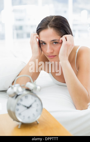 Schwere Frau mit Wecker im Bett liegend Stockfoto