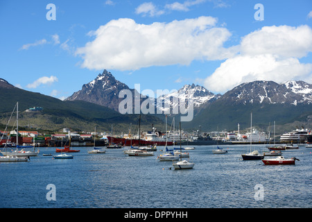 Ushuaia Hafen Monte Olivia Schneebedeckte Berge Segelboote Ushuaia Argentinien | USHUAIA, Argentinien — Segelboote und Frachtschiffe liegen vor Anker im Hafen von Ushuaia, auf dem Beagle-Kanal, während sich die schroffen Gipfel der Fuegischen Andes im Hintergrund erheben. Lange als die südlichste Stadt der Welt vermarktet, dient Ushuaia als Haupthafen für Antarktis-Expeditionskreuzfahrten, etwa 620 Meilen (1.000 km) von der Antarktischen Halbinsel entfernt. Puerto Williams, Chile, auf der gegenüberliegenden Seite des Kanals, streitet diesen Titel nun in Frage. Stockfoto