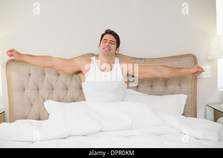 Junger lächelnder Mann streckte die Arme im Bett Stockfoto