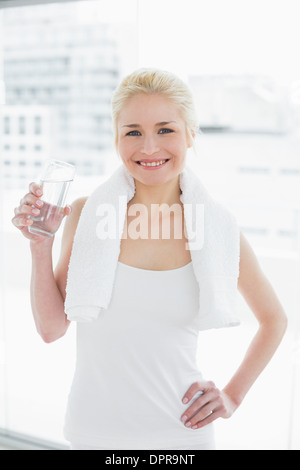 Lächelnde Frau mit einem Glas Wasser im Fitnessraum fit Stockfoto