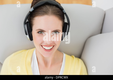 Lächelnde Frau hören von Musik über Kopfhörer auf sofa Stockfoto