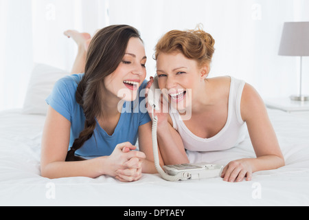 Fröhliche Frau mit Freund mit Telefon im Bett Stockfoto