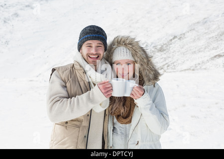 Paar in warme Kleidung mit Kaffeetassen auf verschneiten Landschaft Stockfoto