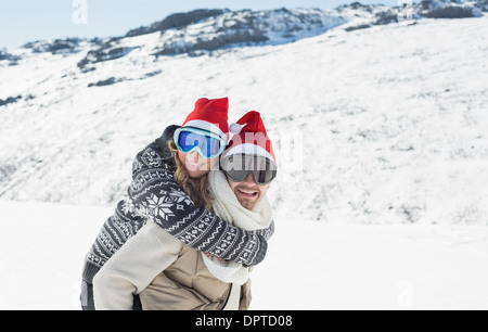 Mann Huckepack stets gut gelaunte Frau auf Schnee Stockfoto