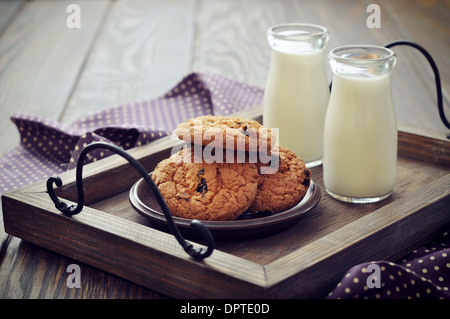 Schokoladenkekse mit Milch in Flaschen auf Tablett aus Holz Stockfoto