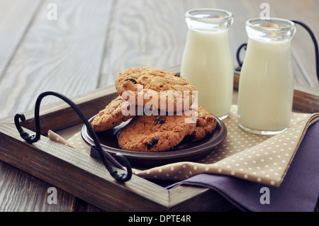 Schokoladenkekse mit Milch in Flaschen auf Tablett aus Holz Stockfoto