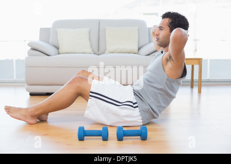 Junge Mann tut Bauch-Crunches im Wohnzimmer Stockfoto