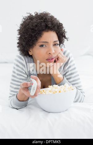 Frau mit Fernbedienung und Popcorn Schüssel im Bett liegend Stockfoto