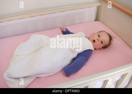 Babymädchen liegen in ihrem Kinderbett in einem Baby-Schlafsack Stockfoto