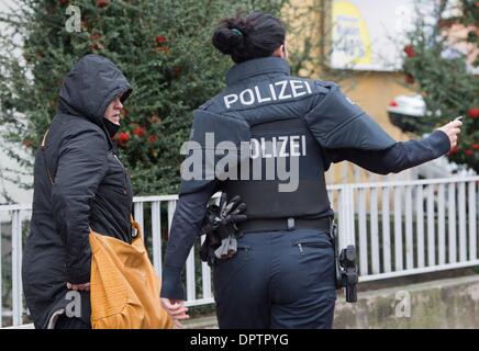 Frankfurt Main, Deutschland. 16. Januar 2014. Ein Polizist leitet eine Frau von einem Mehrfamilienhaus in Frankfurt Main, Deutschland, 16. Januar 2014. Ein 33 Jahre alter Mann verbarrikadiert sich in dem Gebäude mit einer Frau. Der Mann wurde verhaftet. Foto: BORIS ROESSLER/Dpa/Alamy Live News Stockfoto