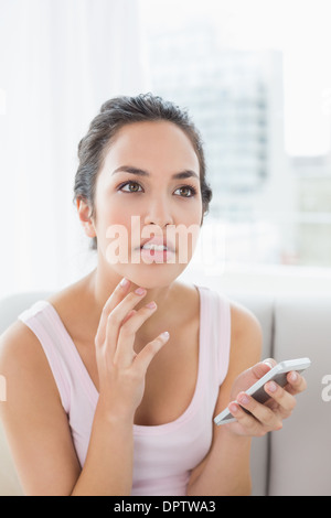 Nachdenkliche Frau mit Handy auf sofa Stockfoto