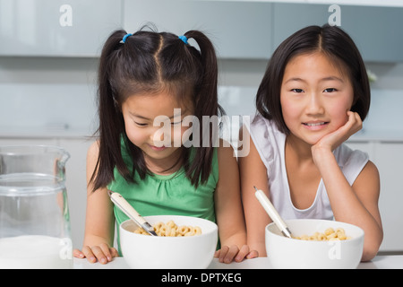 Zwei lächelnde junge Mädchen sitzen mit Schalen in Küche Stockfoto