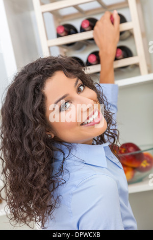 Schöne Frau, eine Flasche Rotwein aus einem Regal zu Hause in ihrer Küche zu wählen Stockfoto